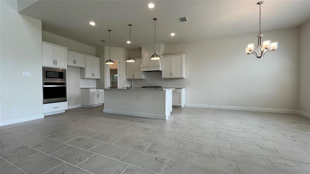 Kitchen featuring white cabinetry, an expansive center island, integrated stainless steel double wall ovens, three brushed metal pendant lights, and large-format tile flooring