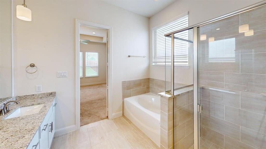 Bathroom featuring a stone countertop vanity, a deep soaking tub with tile surround, a glass-enclosed shower, and large-format tile flooring