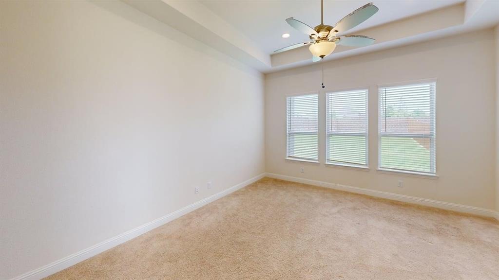 Room featuring a tray ceiling, neutral wall-to-wall carpeting, three windows with horizontal blinds, and a central ceiling fan with an integrated light fixture