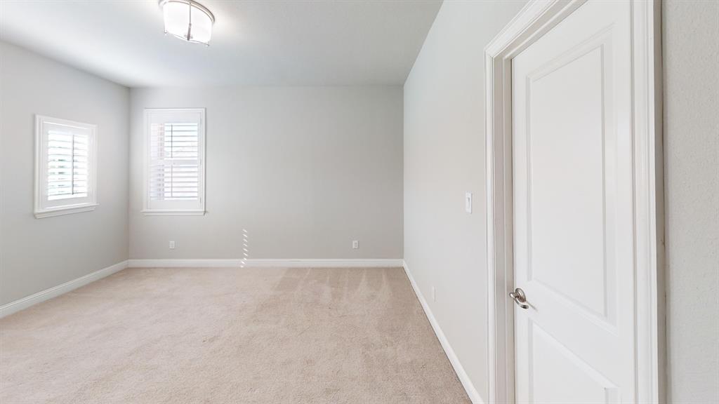 Neutral interior space featuring carpeted flooring, two windows with plantation shutters, a flush-mount light fixture, and a white panel door