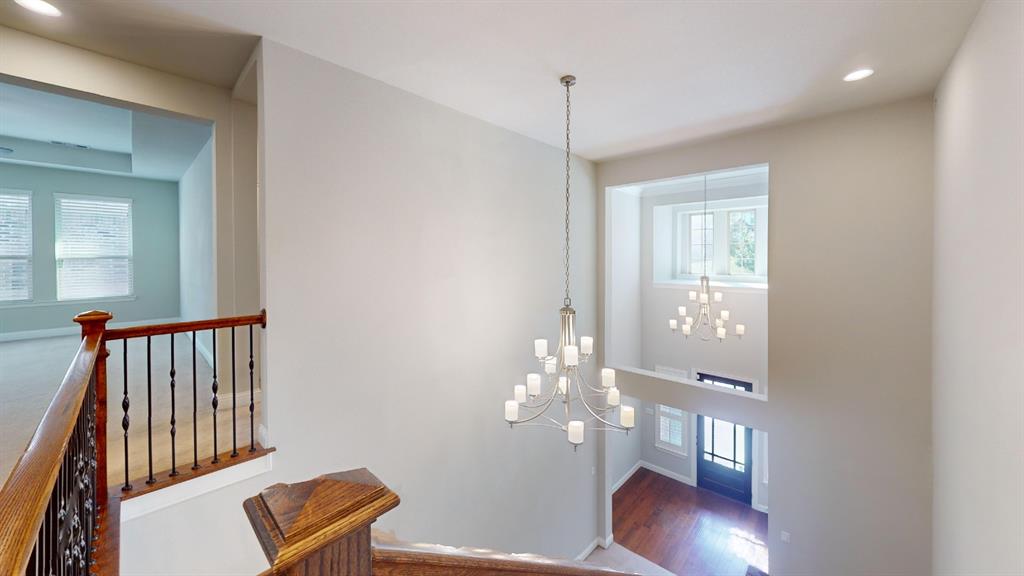 Multi-story foyer featuring a two-tier metal chandelier, wood-finish flooring, and a metal baluster railing with a decorative wood handrail