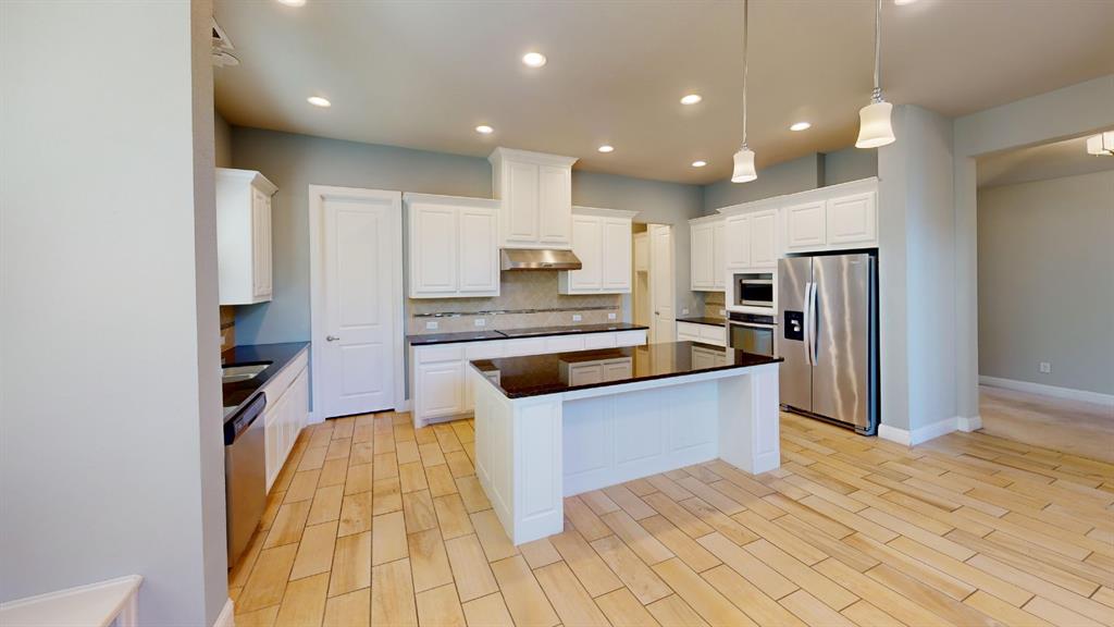 Kitchen featuring white cabinetry, center island with dark countertops, stainless steel appliances, recessed ceiling lighting, and wood-finish tile flooring Kitchen featuring white cabinetry, center island with dark countertops, stainless steel appliances, recessed ceiling lighting, and wood-finish tile flooring