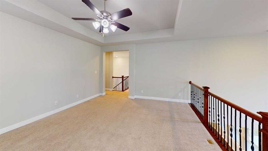 Tray ceiling featuring a central multi-blade ceiling fan with integrated lighting and a decorative balustrade with wood handrails and black metal spindles