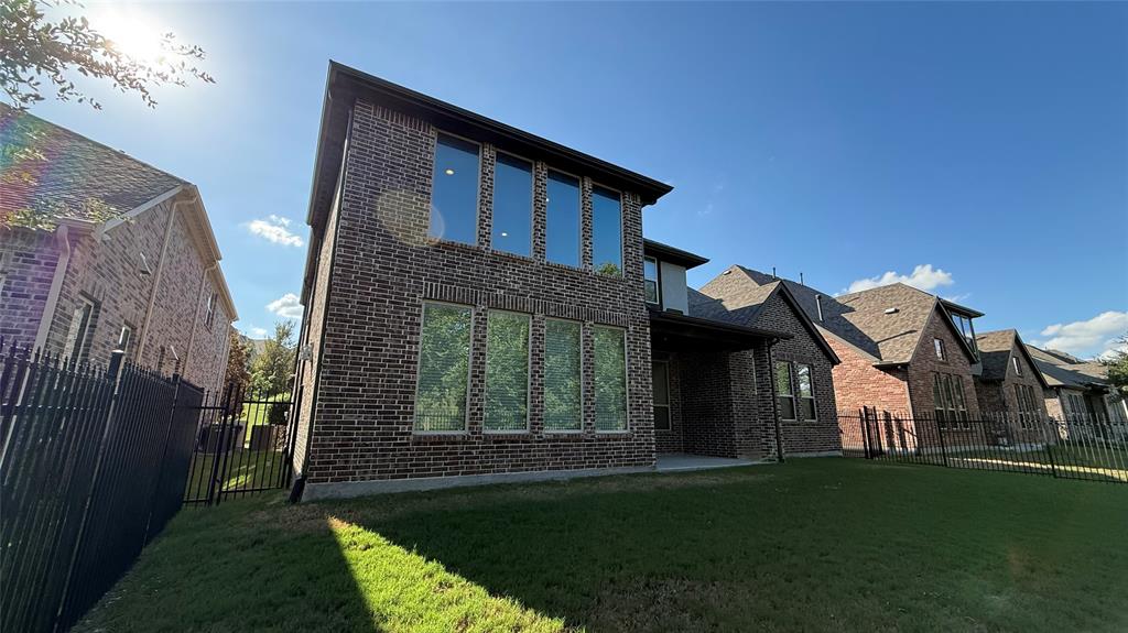 Two-story brick exterior featuring a covered patio, extensive dual-level windows, and fenced backyard