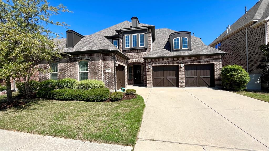 Multi-gabled brick exterior featuring decorative dormer windows, custom-paneled garage doors, and a concrete driveway Multi-gabled brick exterior featuring decorative dormer windows, custom-paneled garage doors, and a concrete driveway