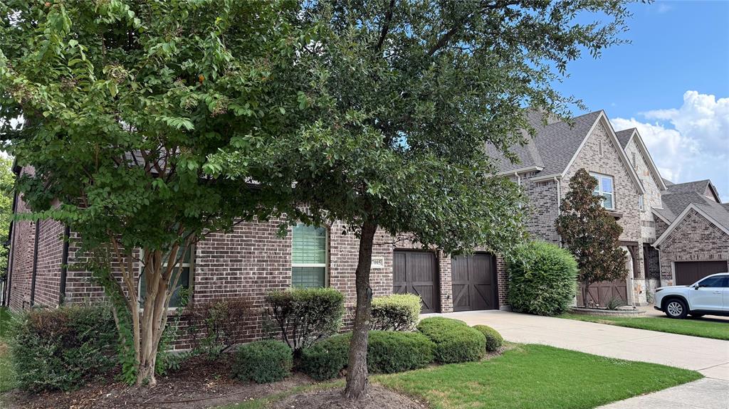 Multi-level brick exterior featuring a steeply pitched roofline, wood-finish garage doors, and a concrete driveway Multi-level brick exterior featuring a steeply pitched roofline, wood-finish garage doors, and a concrete driveway