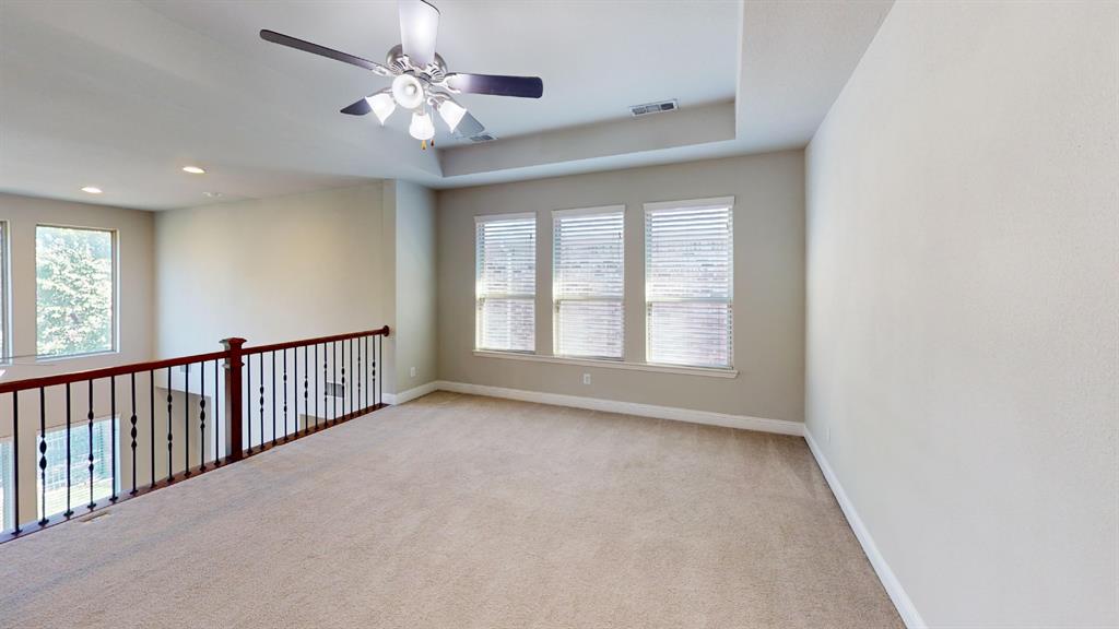 Tray ceiling featuring a central multi-light ceiling fan, neutral carpeting, and a wooden handrail with metal balusters