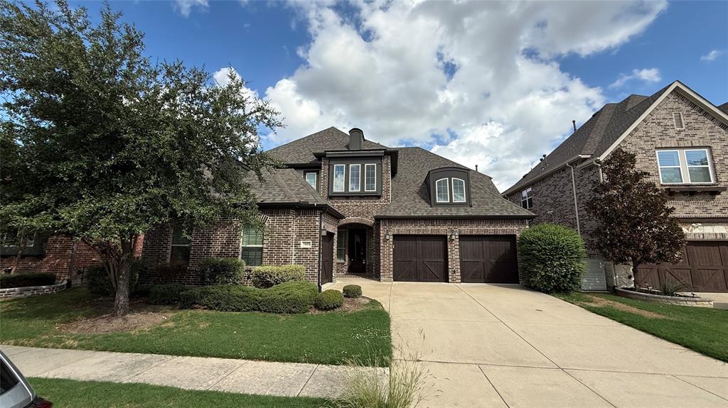Two-story brick exterior featuring a multi-gabled roofline, dormer window, integrated two-car garage with carriage-style doors, and manicured landscaping Two-story brick exterior featuring a multi-gabled roofline, dormer window, integrated two-car garage with carriage-style doors, and manicured landscaping