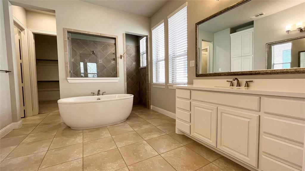 Freestanding soaking tub, vanity with solid surface countertop, large framed wall mirror, tile flooring, and walk-in shower with tiled surround