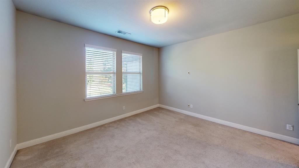 Neutral-toned interior space featuring light-colored wall-to-wall carpeting, dual windows with horizontal blinds, and a circular flush-mount ceiling light fixture