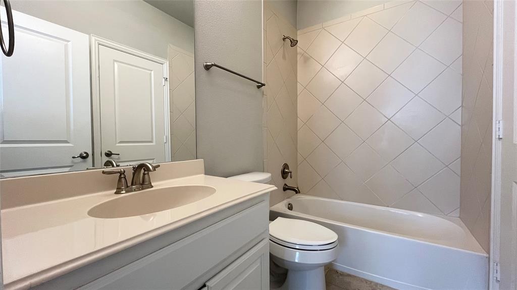 Bathroom featuring a vanity with an integrated basin, countertop-mounted metal faucet, diagonal tile wall surround, and combination tub-shower with metal fixture