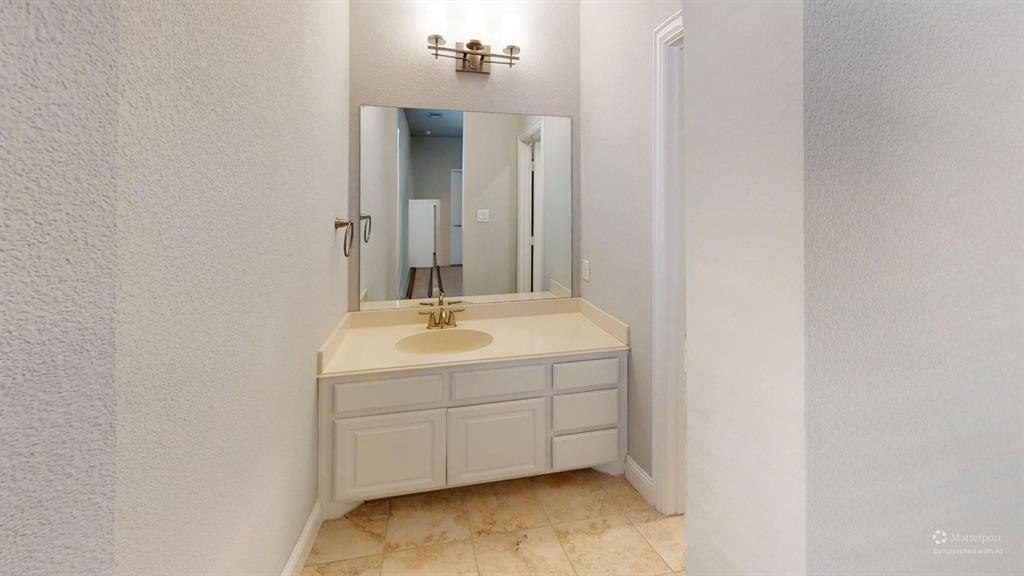 Bathroom vanity featuring a solid surface countertop, an integrated oval basin, light-toned cabinetry, a wall-mounted mirror, and stone-tile flooring