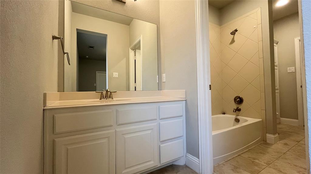 Bathroom featuring a white vanity cabinet with an integrated countertop, large wall-mounted mirror, and tub-shower combination with diagonal tile surround