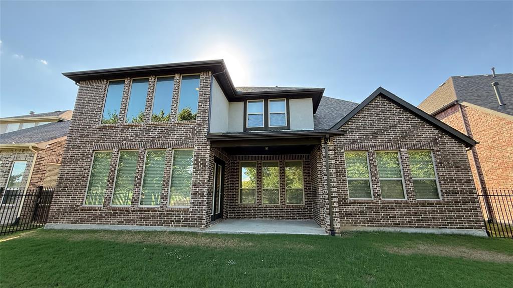 Two-story brick exterior featuring a covered patio, multi-pane windows, and black metal perimeter fencing