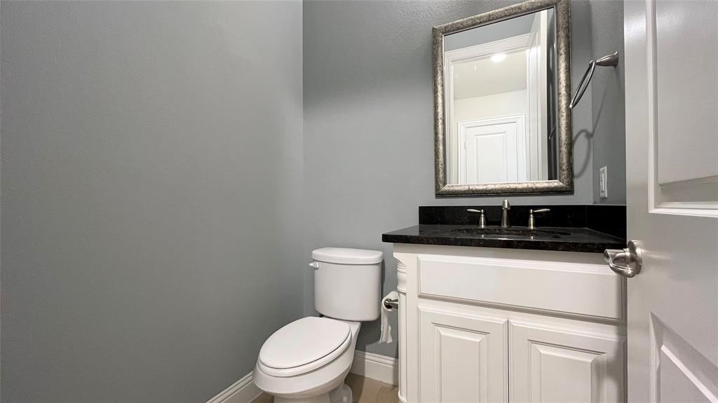 White cabinetry vanity with a dark stone countertop, integrated sink, wall-mounted mirror, and chrome hardware