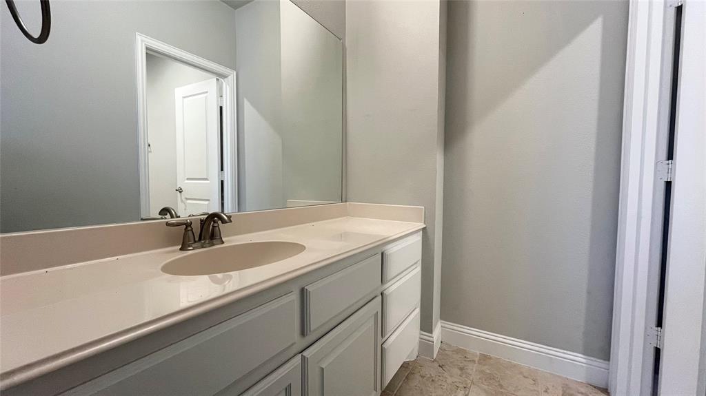 Vanity featuring light-toned cabinetry, an integrated oval sink, stone-finish countertop, polished metal faucet, and wall-to-wall mirror with stone-finish tile flooring