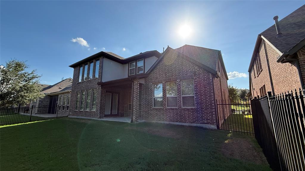 Multi-story brick exterior featuring a covered patio, expansive windows, and a metal perimeter fence