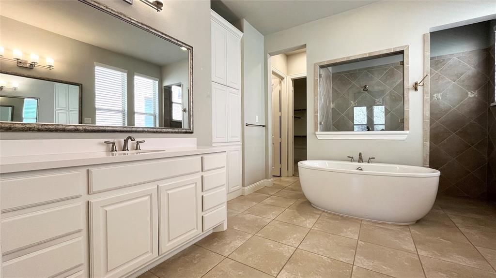Bathroom featuring a double-sink vanity with white cabinetry, quartz countertop, freestanding soaking tub, and tile flooring