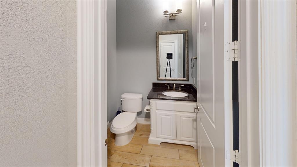 White vanity cabinet featuring a dark stone countertop, undermount oval sink, stone-finish flooring, and wall-mounted vanity lighting