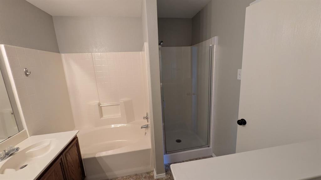 Bathroom featuring a separate soaking tub and glass-enclosed shower stall, wood-finish vanity cabinet, integrated sink, and wall-mounted mirror
