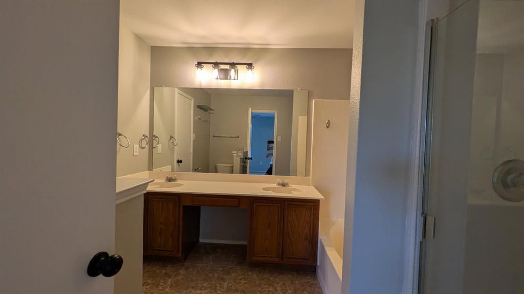 Double vanity with inset sinks, wood-finish cabinetry, full-width vanity mirror, tri-light fixture, and tiled shower enclosure