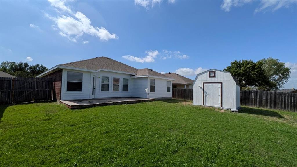 Rear exterior featuring a concrete patio, white horizontal siding, a pitched shingle roof, and a detached storage shed set within a fenced yard