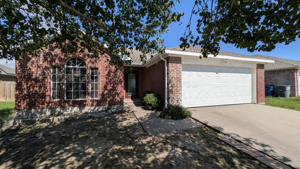 Single-story residence with red brick exterior, multi-pane arched window, concrete driveway, and attached two-car garage