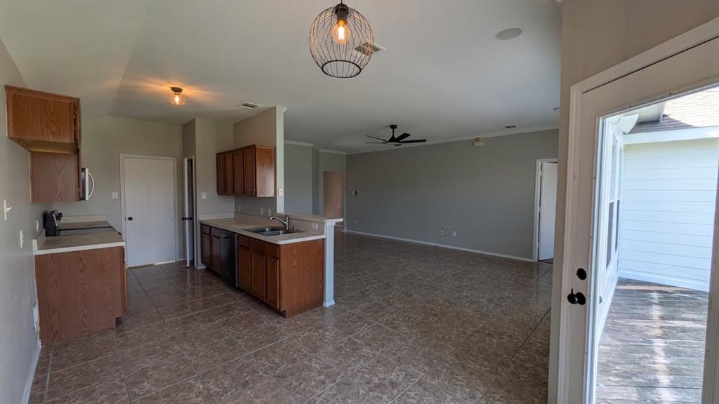 Open-concept interior featuring tile flooring, wood cabinetry, stainless steel sink with pull-down faucet, cage-style pendant lighting, and ceiling fan Open-concept interior featuring tile flooring, wood cabinetry, stainless steel sink with pull-down faucet, cage-style pendant lighting, and ceiling fan
