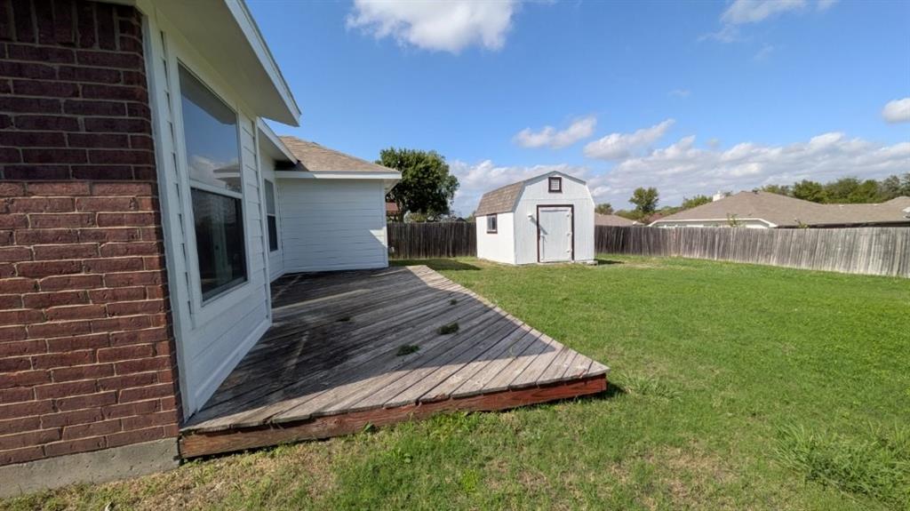 Rear exterior featuring a wood deck, lawn, detached storage structure, and perimeter fencing