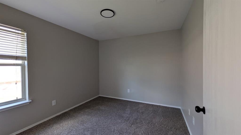 Neutral-toned interior space featuring neutral wall paint, wall-to-wall carpeting, a window with horizontal blinds, and a circular flush-mount ceiling light fixture