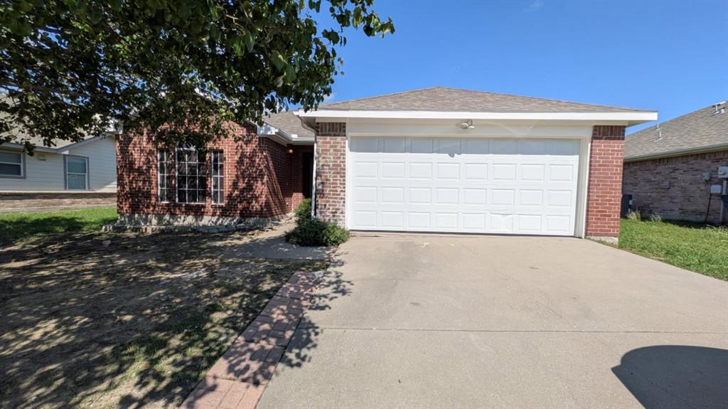 Single-story residence featuring a brick exterior, shingled roof, attached two-car garage, concrete driveway, and front-facing multi-pane windows Single-story residence featuring a brick exterior, shingled roof, attached two-car garage, concrete driveway, and front-facing multi-pane windows