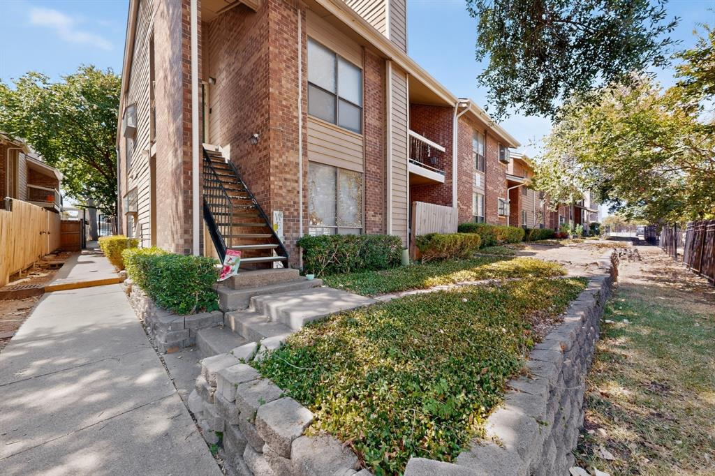 Brick exterior with vertical siding accents, concrete walkways, mature trees, and a metal staircase with railing