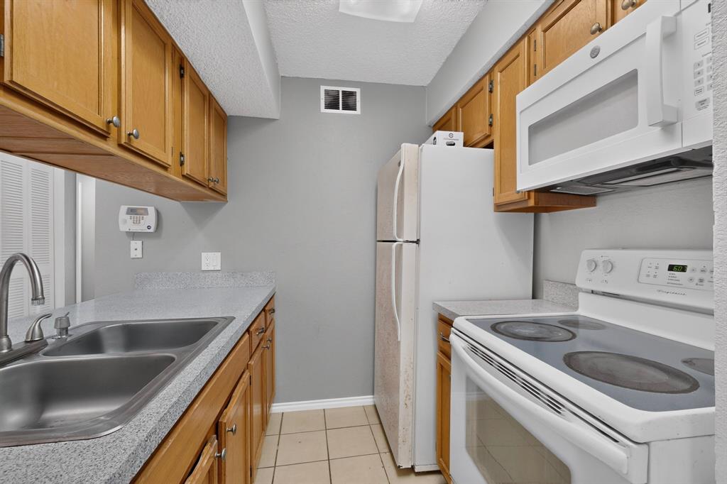 Kitchen featuring wood cabinetry, a double basin stainless steel sink, light-toned countertops, and tile flooring