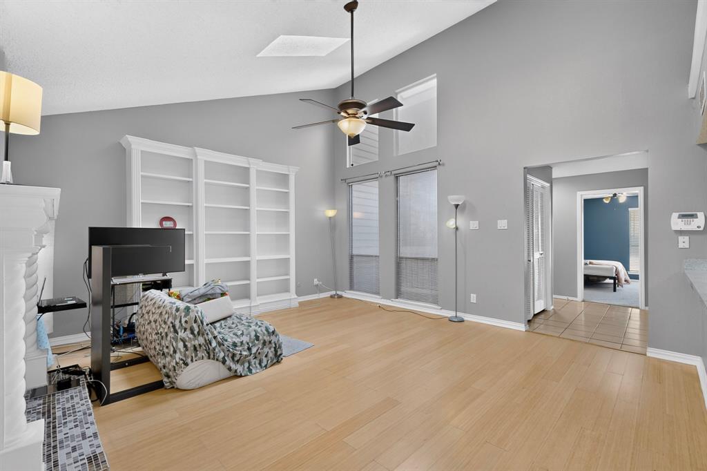 Vaulted ceiling with a ceiling fan, recessed windows, wood-finish flooring, built-in shelving, and a tiled fireplace surround