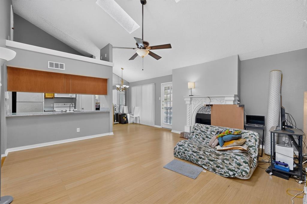 Vaulted ceilings, wood-finish flooring, a decorative fireplace, and an open-concept pass-through to the kitchen with a breakfast bar