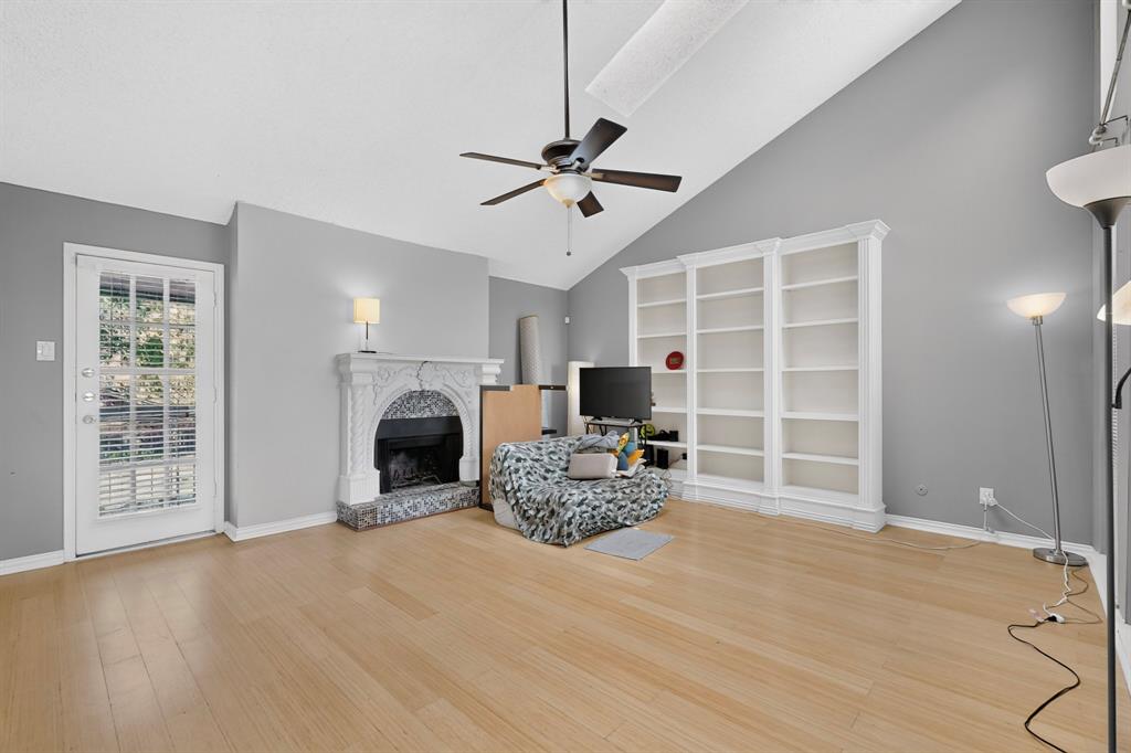 Vaulted ceiling, wood-finish flooring, ceiling fan, ornate fireplace with a marble-finish surround, and built-in shelving