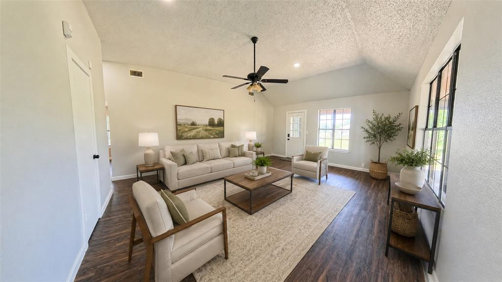 Living area featuring vaulted ceilings, wood-finish flooring, a ceiling fan, and large windows with black frames