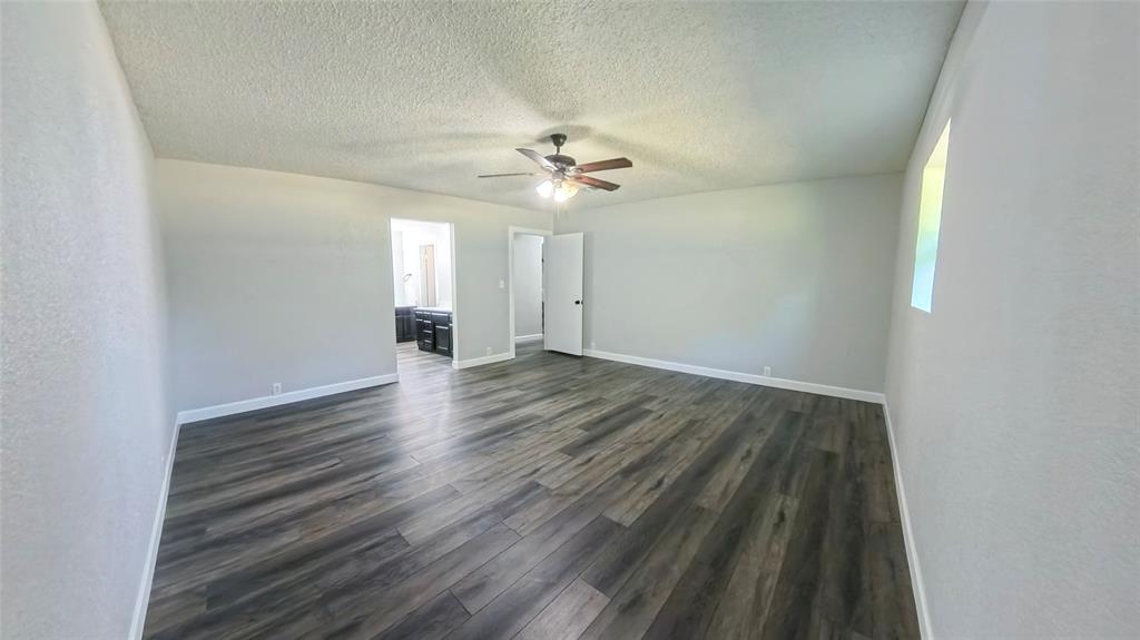 Spacious interior featuring wood-finish flooring, a ceiling fan with light fixture, and textured ceilings