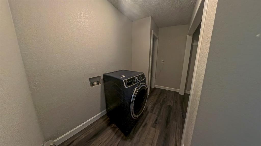 Utility area featuring wood-finish flooring, textured walls, and a recessed plumbing connection