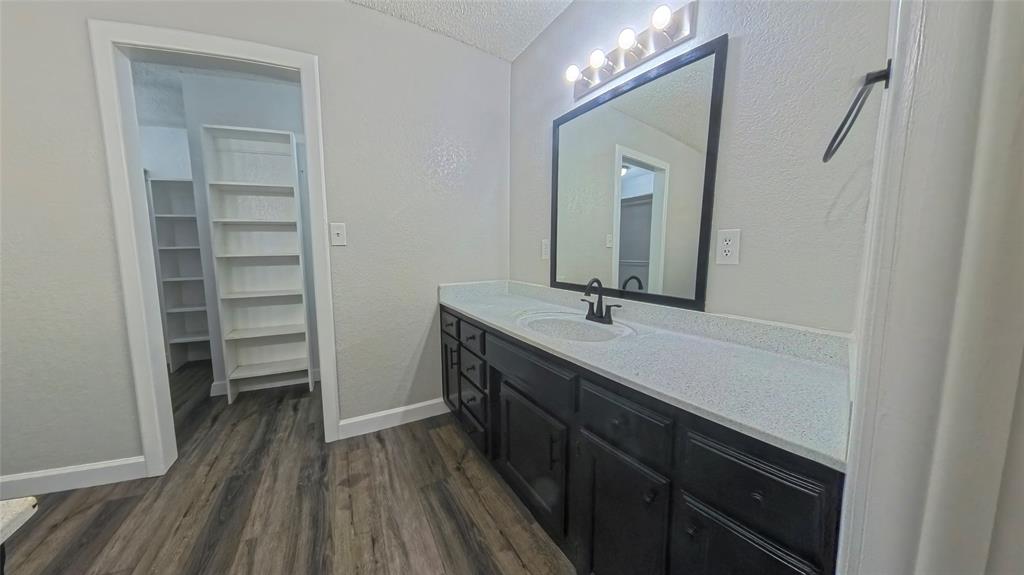 Bathroom featuring a dark wood-finish vanity with a stone countertop, an integrated oval sink, black hardware, and wood-finish flooring