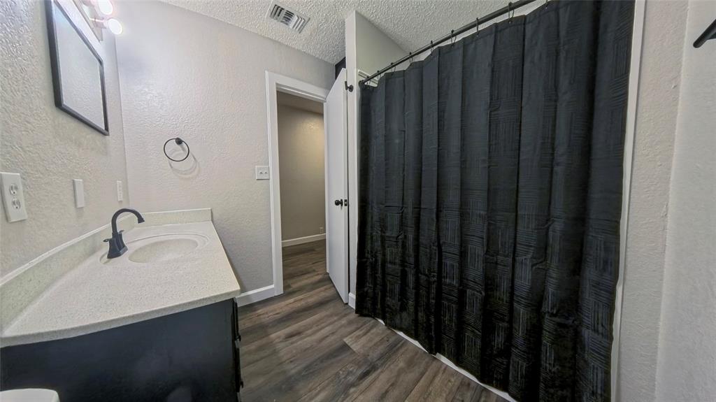 Bathroom featuring a stone-composite countertop with an integrated basin, matte black faucet, dark-finish cabinetry, and wood-finish flooring