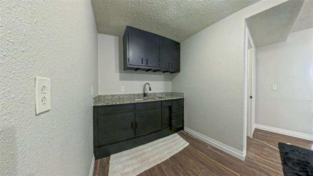 Dark cabinetry featuring built-in storage, stone-finish countertop, undermount sink with goose-neck faucet, and wood-finish flooring