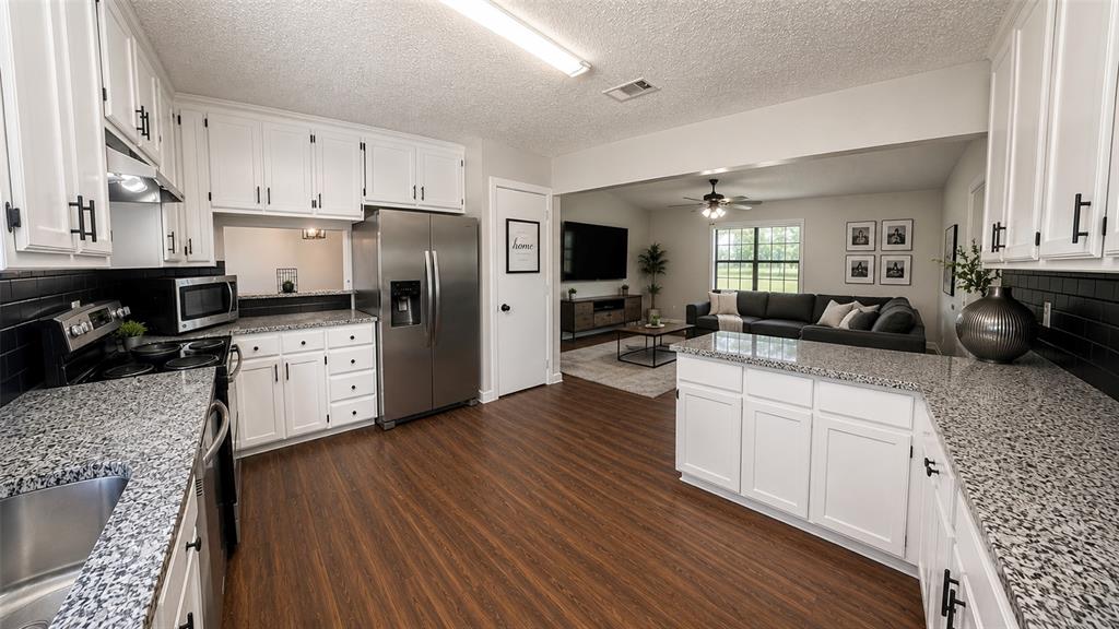 Kitchen featuring white cabinetry with matte black hardware, stone-finish countertops, black tile backsplash, stainless steel appliances, and wood-finish flooring Kitchen featuring white cabinetry with matte black hardware, stone-finish countertops, black tile backsplash, stainless steel appliances, and wood-finish flooring