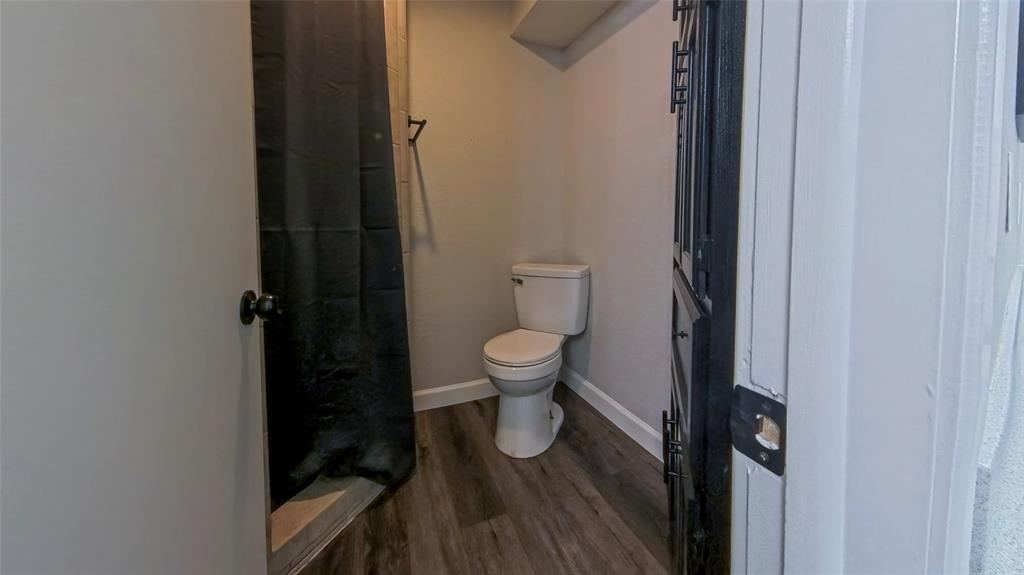 Bathroom featuring wood-finish flooring, a two-piece toilet, and a built-in cabinet with matte black hardware
