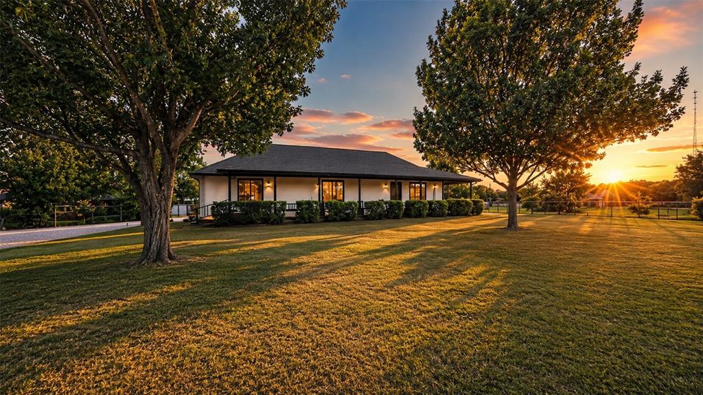 Exterior featuring a covered wrap-around porch, stucco siding, a hip roof, and expansive lawn with mature trees Exterior featuring a covered wrap-around porch, stucco siding, a hip roof, and expansive lawn with mature trees