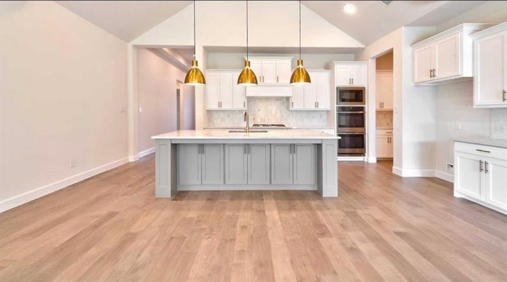 Vaulted ceilings, kitchen island with stone countertops, wood-finish flooring, shaker-style cabinetry, and recessed wall-mounted ovens