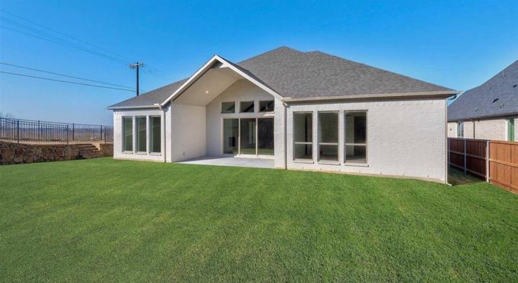 Rear exterior featuring a brick facade, covered patio, expansive lawn, multi-pane windows, and a stone retaining wall