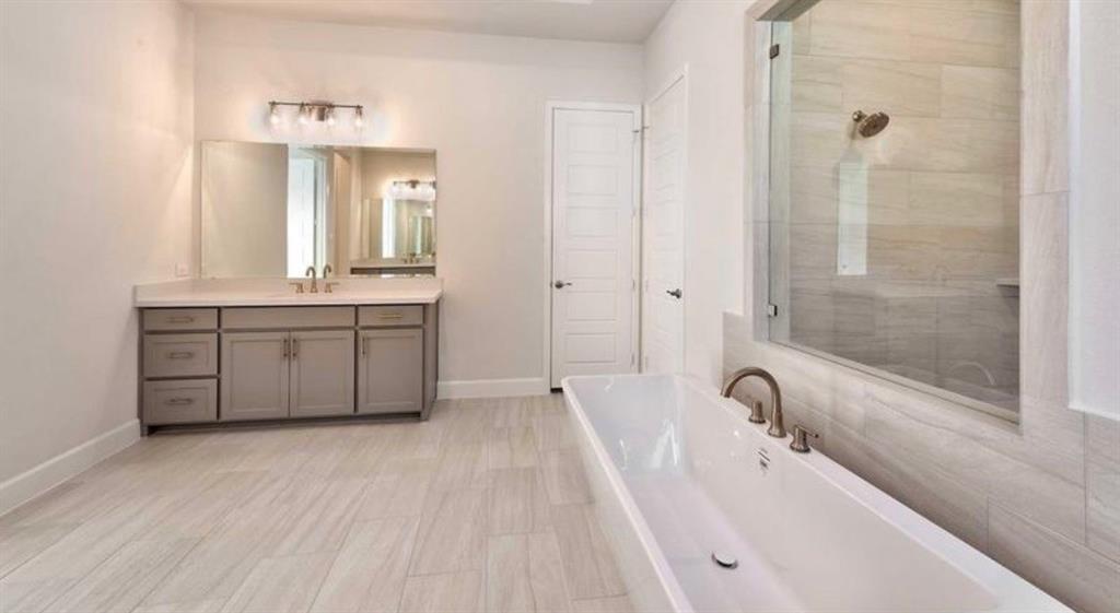 Freestanding soaking tub with a deck-mounted faucet, walk-in tile shower with a glass enclosure, dual-sink vanity with light-toned cabinetry, and large-format tile flooring