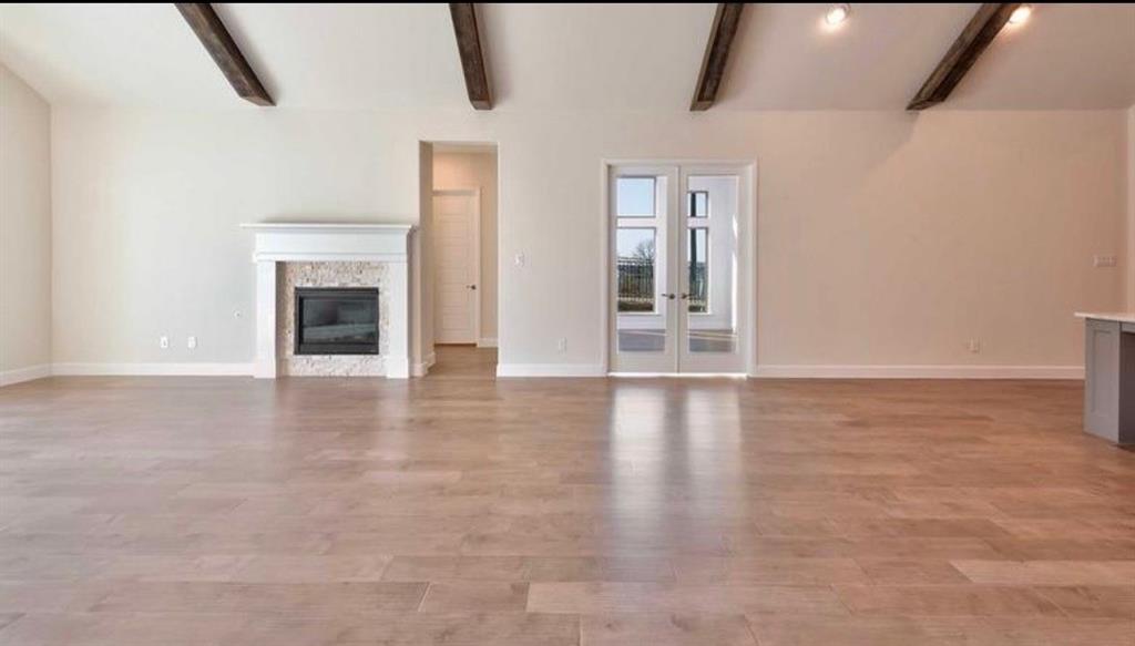 Vaulted ceiling featuring exposed wood beams, wood-finish flooring, fireplace with stone surround and mantle, and French doors