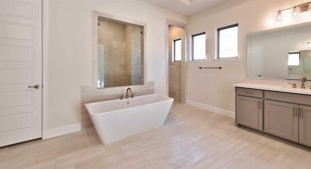 Freestanding soaking tub, walk-in tile surround shower, dual-sink vanity with neutral cabinetry, large-format tile flooring, and oversized wall-mounted mirror